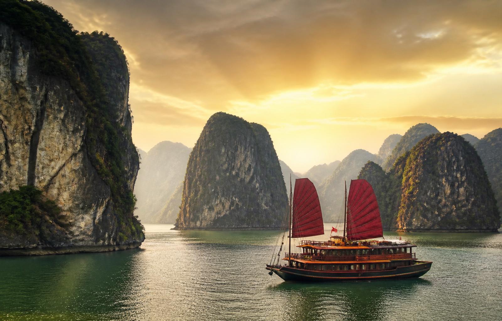 Ha Long Bay at golden hour with traditional red-sail junk boat